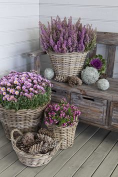 three wicker baskets filled with flowers sitting on top of a wooden floor next to a bench