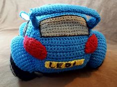 a crocheted blue toy car sitting on top of a bed next to a pillow