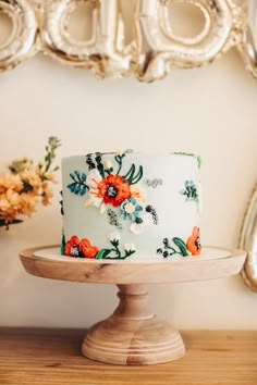 a white and blue cake with flowers on it sitting on a wooden stand in front of a mirror