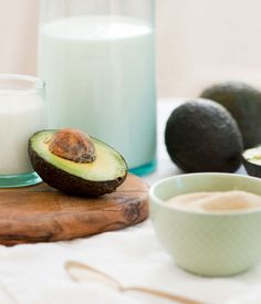 an avocado on a cutting board next to a glass of milk and some fruit