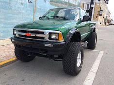 a green pick up truck parked in front of a wall with a mural on it