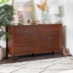 a wooden dresser sitting next to a window with plants on top of it in a living room