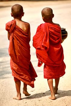 two men in red robes walking down the street with their backs turned to the camera