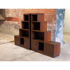 two bookshelves sitting next to each other in front of a brick wall and cement floor