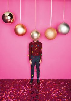 a man standing in front of a pink wall with christmas ornaments hanging from the ceiling