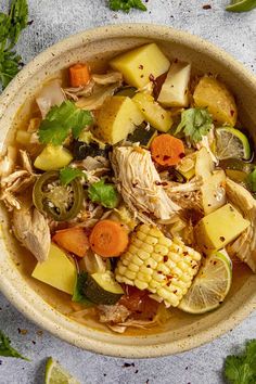 a bowl filled with chicken, corn, and potatoes next to cilantro leaves