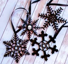 three metal snowflakes on a white wooden surface with ribbon and bow hanging from them