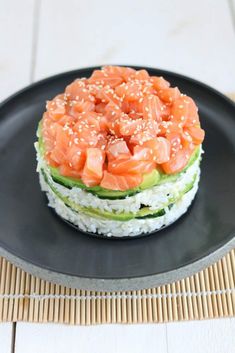 a black plate topped with sushi and cucumber next to a bamboo mat