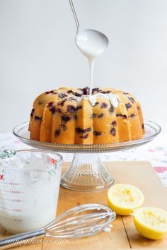 a cake is being drizzled with icing on a wooden table next to lemons and a measuring cup