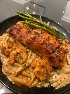 a black plate topped with chicken and pasta covered in gravy next to asparagus