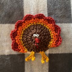 a crocheted turkey sitting on top of a checkered table cloth with eyes