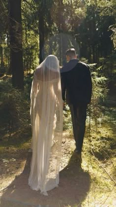 the bride and groom are walking through the woods in their wedding gowns, veils over their heads