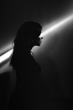 a woman standing in the dark with her head turned to the side and lights behind her