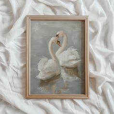 a painting of two swans in water on a white bed sheet, with a gold frame