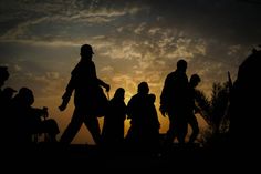 silhouettes of people walking in front of the sun at dusk or dawn with clouds