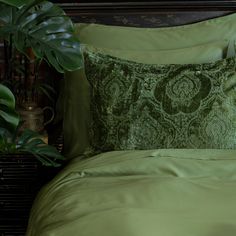 a bed with green sheets and pillows next to a potted plant