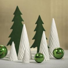 green and white ornaments are lined up in front of small christmas trees on a table