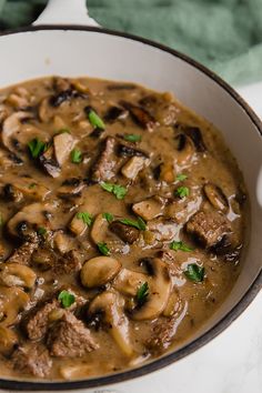 a bowl filled with meat and mushroom soup on top of a white countertop next to a green towel