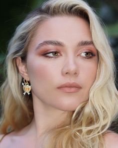 a woman with long blonde hair wearing gold and red makeup looks at the camera while posing for a photo