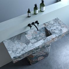 a marble sink with three soap dispensers on the top and two bottles next to it