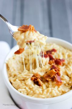 a spoon full of macaroni and cheese with bacon on top is being lifted from the bowl