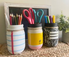 three mason jars with pencils, scissors and markers in them sitting on a table