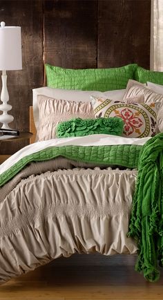 a bed with green and white comforters in a room next to a lamp on a table