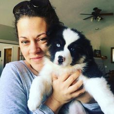 a woman holding a black and white dog in her arms with sunglasses on it's head