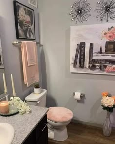 a bathroom decorated in pink and white with flowers on the counter, toilet seat cover