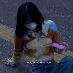 a woman sitting on the ground wearing a face mask and holding a pink toothbrush