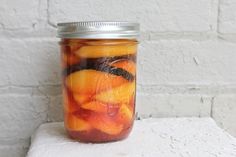 a mason jar filled with sliced fruit sitting on top of a white brick wall,