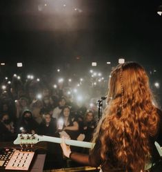 a woman with long hair playing an electric guitar in front of a group of people