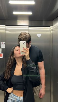 a man and woman taking a selfie in front of an elevator with their cell phone