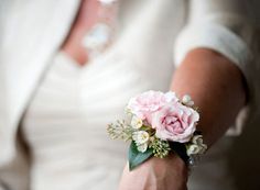 a woman wearing a white jacket holding a pink rose and greenery wrist corsage