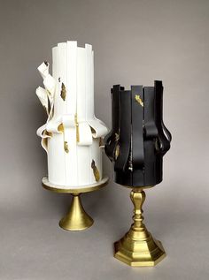 two white and black cakes sitting next to each other on top of gold pedestals