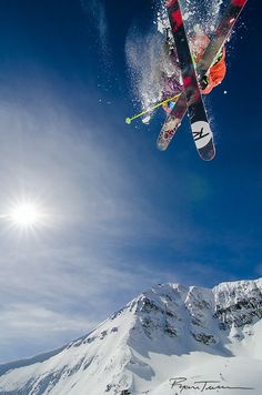 a person on skis jumping in the air over snow covered mountains and trees with bright sun behind them