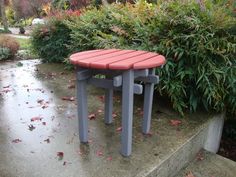 a red and gray bench sitting on top of a cement step next to bushes with leaves