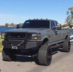 a large gray truck driving down a street next to a body of water on a sunny day