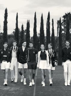 black and white photograph of men and women in tennis uniforms walking on court with trees behind them