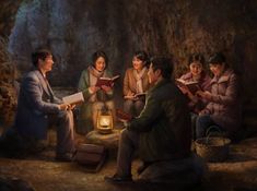 a group of people sitting around a lantern in a cave, reading and looking at each other