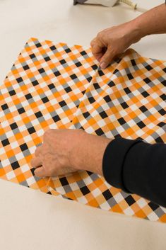 a person is cutting up an orange and black checkered fabric on the table top