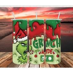 three green and red grinade sodas sitting on top of a wooden table next to the ocean