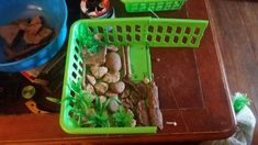 a green basket filled with food on top of a wooden table next to two blue buckets