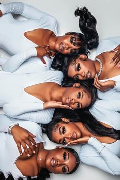 four beautiful women laying on top of each other in white outfits, posing for the camera