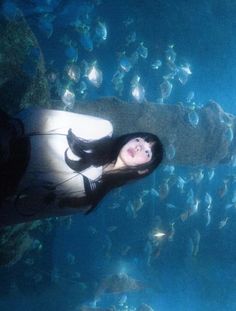 a woman standing in front of a large aquarium filled with lots of fish and looking up at the camera