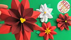 someone is holding some paper flowers on a green surface with red, white and yellow petals