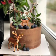 a chocolate cake decorated with deer figurines and blueberries on a window sill