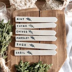 five wooden spoons with words on them sitting on a cutting board next to herbs