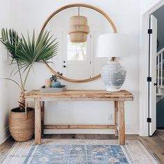 a wooden table sitting under a round mirror next to a plant on top of a rug