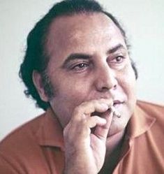 a man in an orange shirt is holding his hand to his chin and looking at the camera